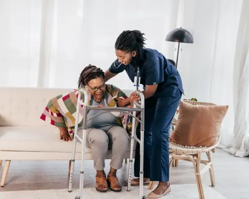 Verpleegster helpt oudere vrouw opstaan van bank