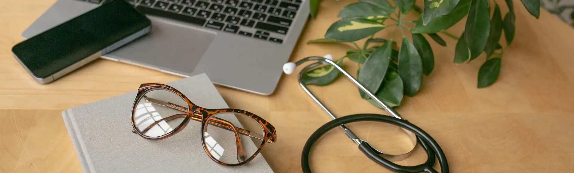 Laptop, notitieboekje, bril, mobiel en stethoscoop op een bureau Laptop, notitieboekje, bril, mobiel en stethoscoop op een bureau