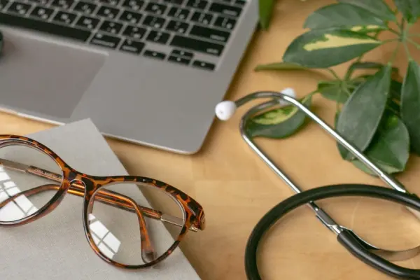 Laptop, notitieboekje, bril, mobiel en stethoscoop op een bureau