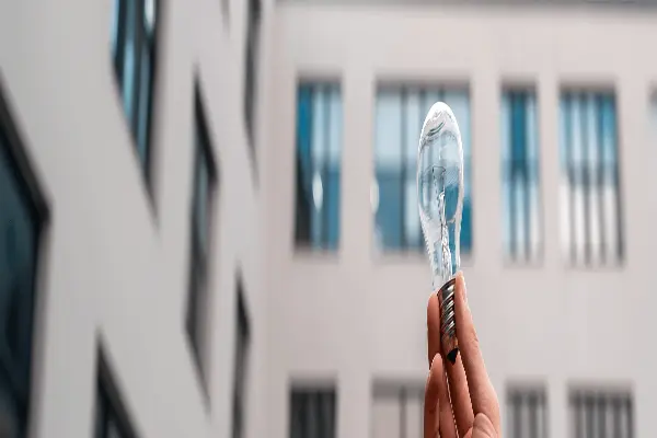 Żarówka trzymana w dłoni na tle elewacji budynku. Audyt energetyczny budynku. 