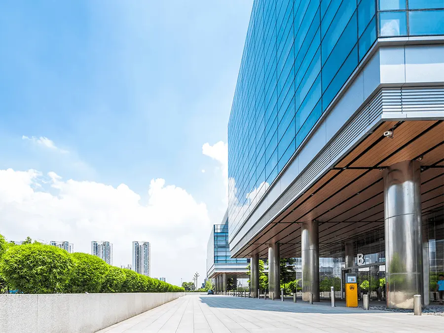 Nowoczesny budynek biurowy z przestrzenią dla pieszych i zielenią wokół, zaprojektowany z myślą o komforcie i dobrostanie użytkowników zgodnie ze standardem WELL. 