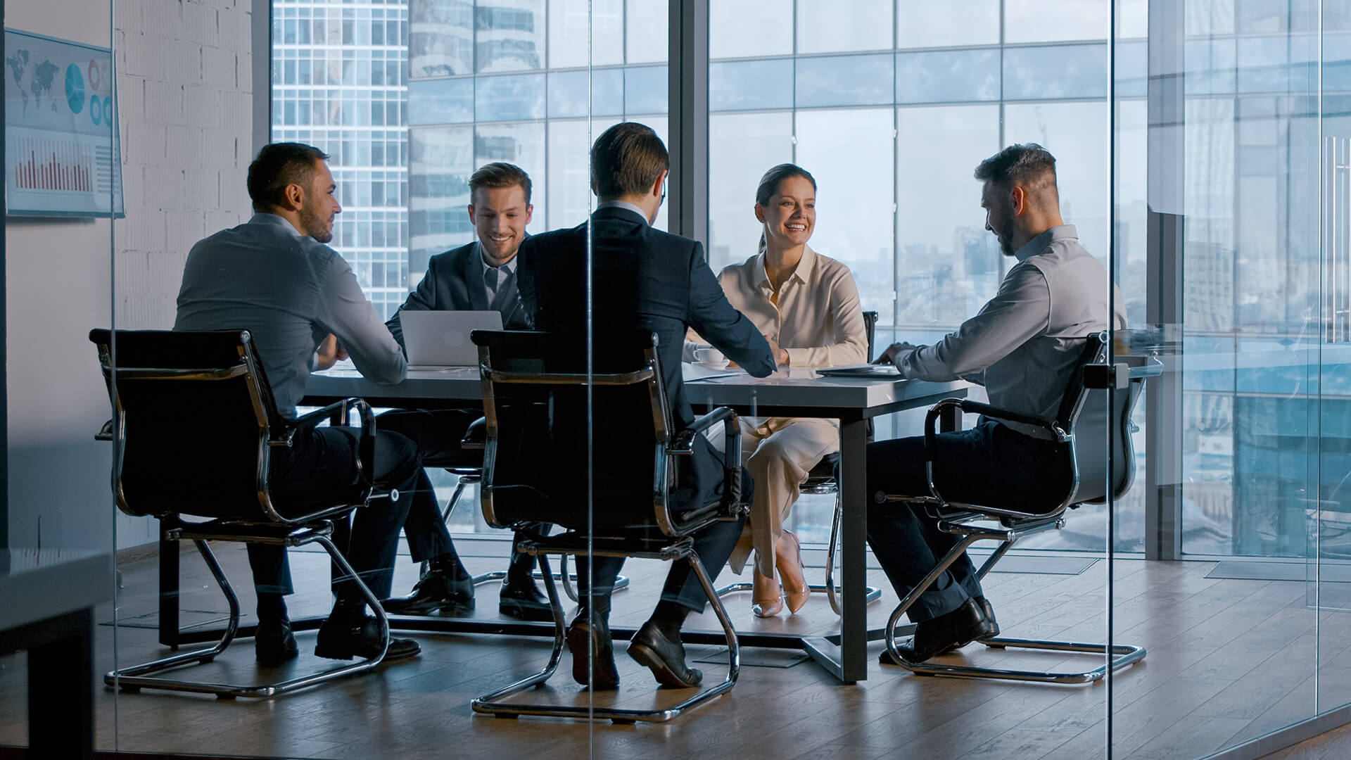 Grupa eleganko ubranych ludzi siedżacych przy stole w sali konferencyjnej.