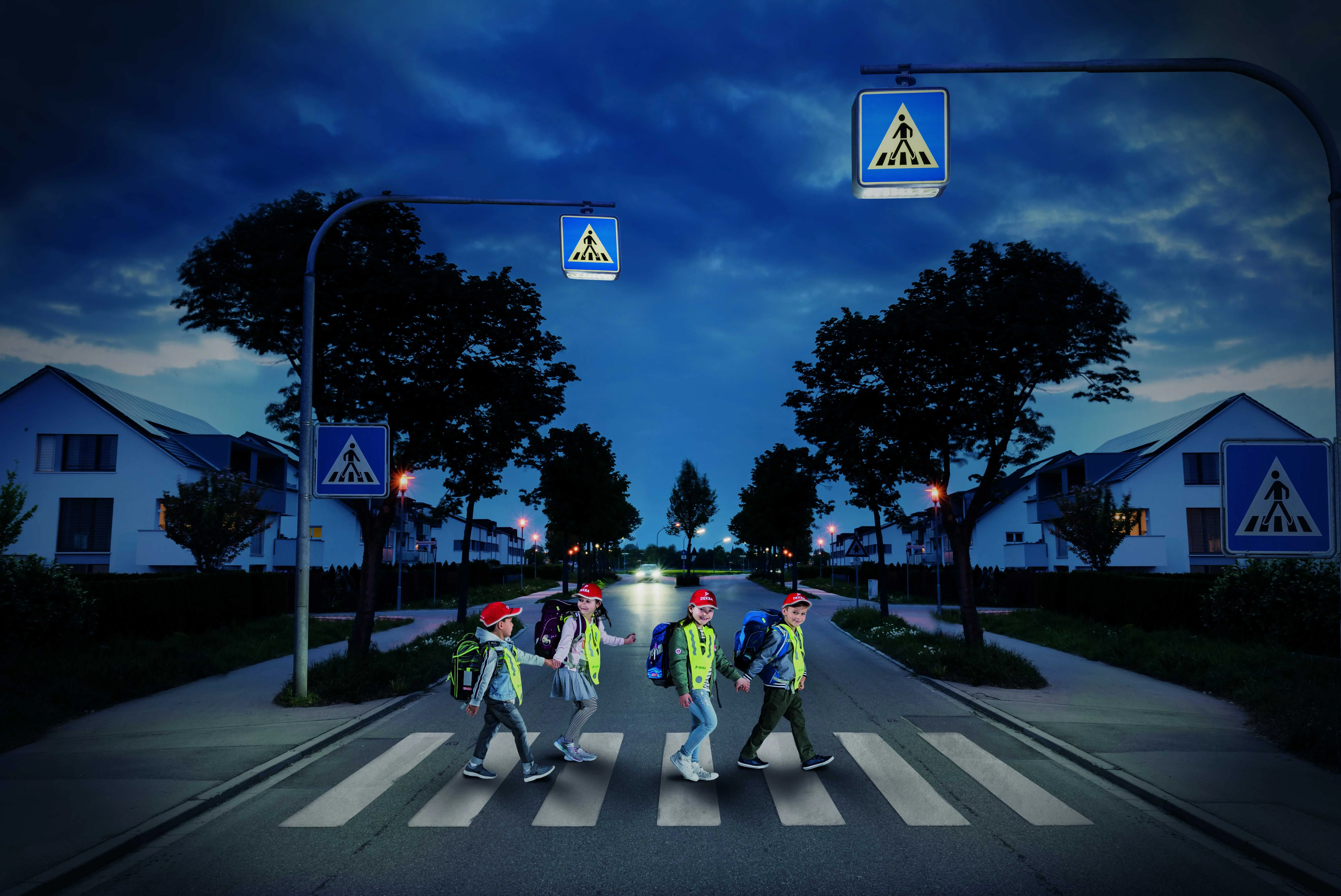 Bezpieczeństwo dzieci na drogach - odblaskowe czapeczki DEKRA Dzieci przechodzące przez ulicę po zmierzchu w odblaskowych czapeczkach DEKRA
