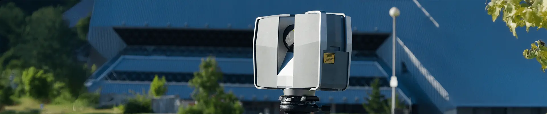 Urządzenie do skanowania laserowego ustawione przed budynkiem w cele dokonania inwentaryzacji budynku 3D.