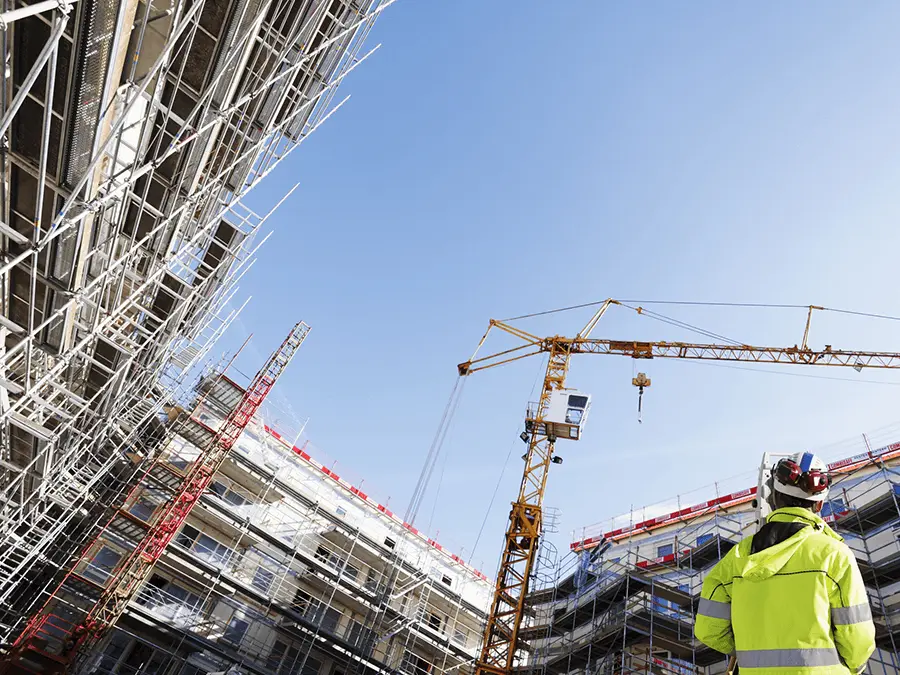 Inżynier BREEAM na placu budowy z dźwigami i powstającym budynkiem w tle, nadzorujący realizację inwestycji budowlanej. 