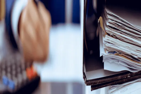 Segregator z dokumentami na biurku oraz osoba wypełniająca formularze. Kontrola dokumentacji na potrzeby ubezpieczenia IDI