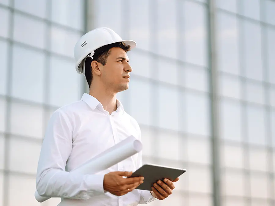 Inżynier z dokumentacją na tle przeszklonego obiektu, kontroluje jakość wykonania robót budowlanych.
