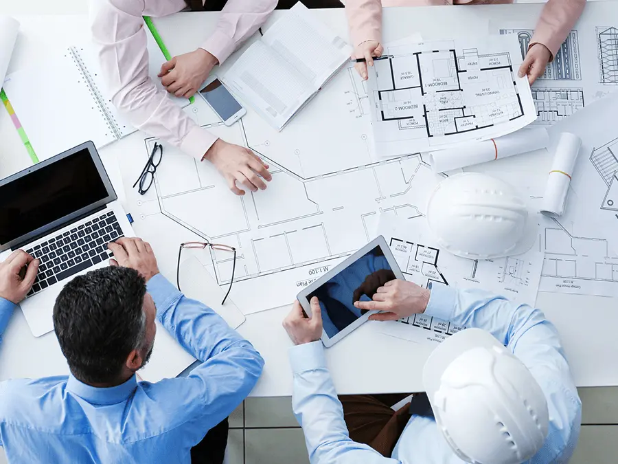 Zespół inżynierów analizujących na stole dokumentację. Koordynacja BHP na placu budowy.