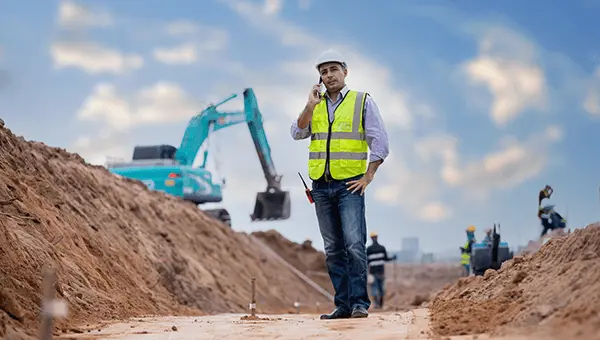 Inżynier na placu budowy z maszynami i dźwigiem w tle. Realizacja inwestycji budowlanej.