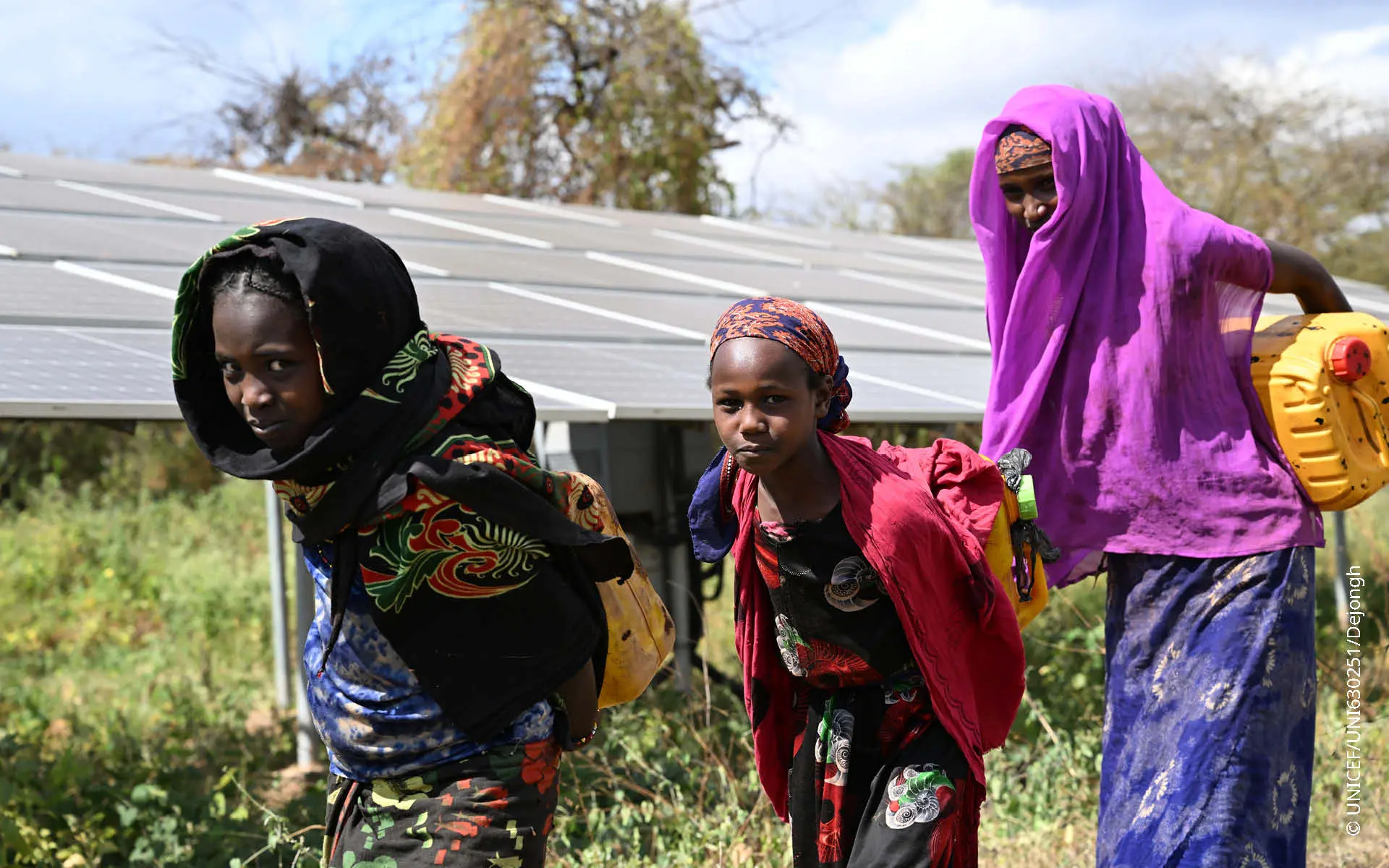 Three Ethiopien women carrying fresh water in canisters on their backs.