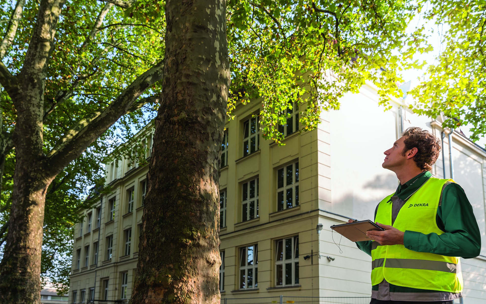 A DEKRA employee holding a clipboard looks at a building A DEKRA employee holding a clipboard looks at a building