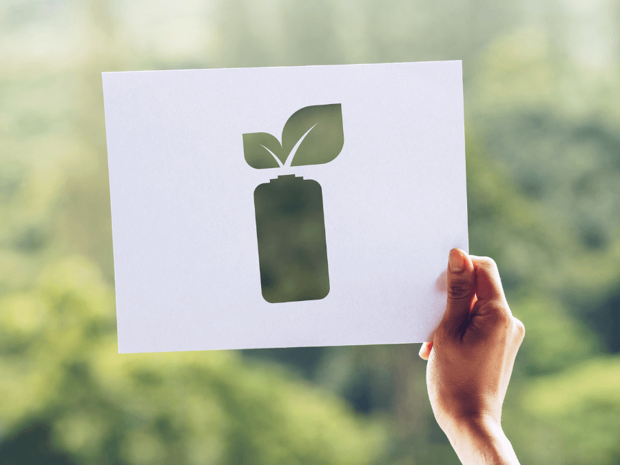 a hand holding a paper with a battery cut out in front of a green field a hand holding a paper with a battery cut out in front of a green field