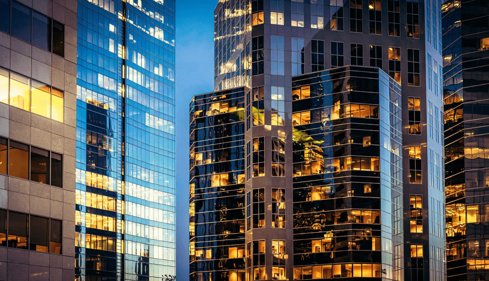 Office lights illuminating a collection of modern downtown office towers after sunset.