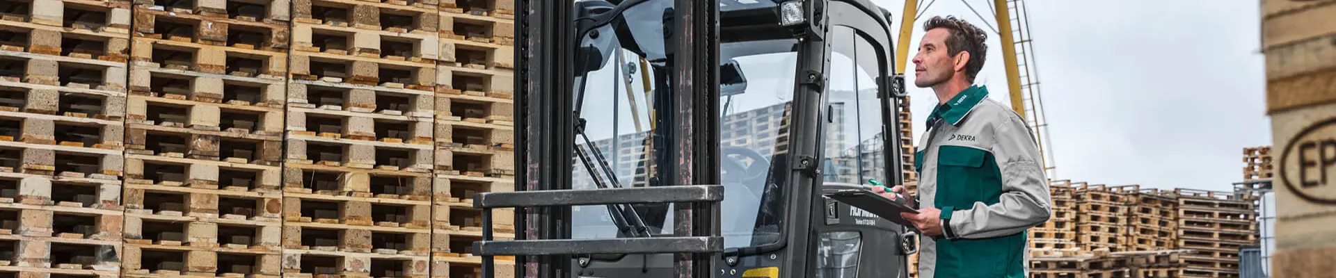 A DEKRA expert stands next to a forklift in the outdoor pallet storage area