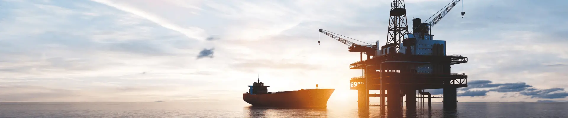 An oil platform and a ship on the ocean with a sunset in the background.