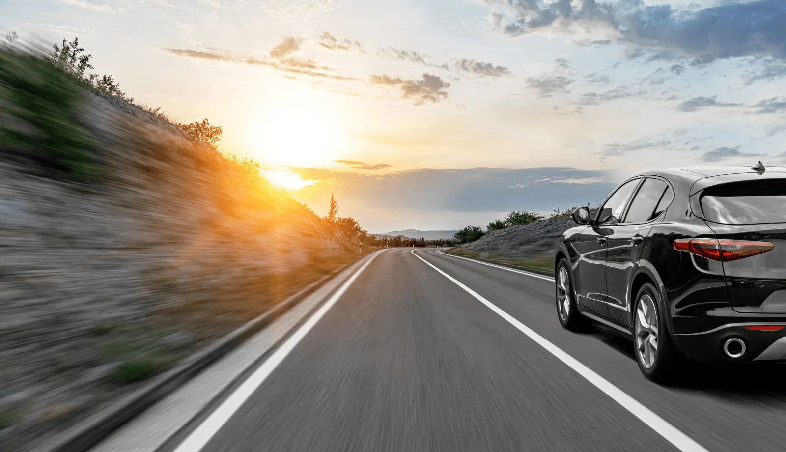 A gray car drives on a scenic road, surrounded by a natural landscape in the rays of sunset or dawn.
