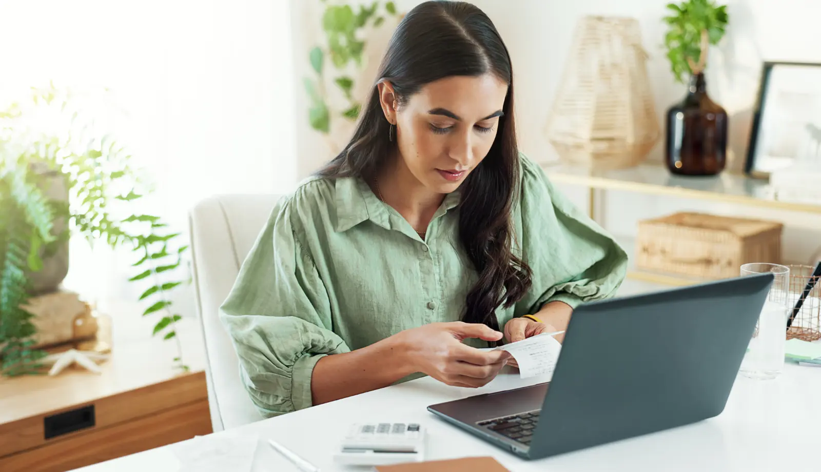 Woman sitting in front of an open laptop, holding a document while reviewing sustainability reporting information.