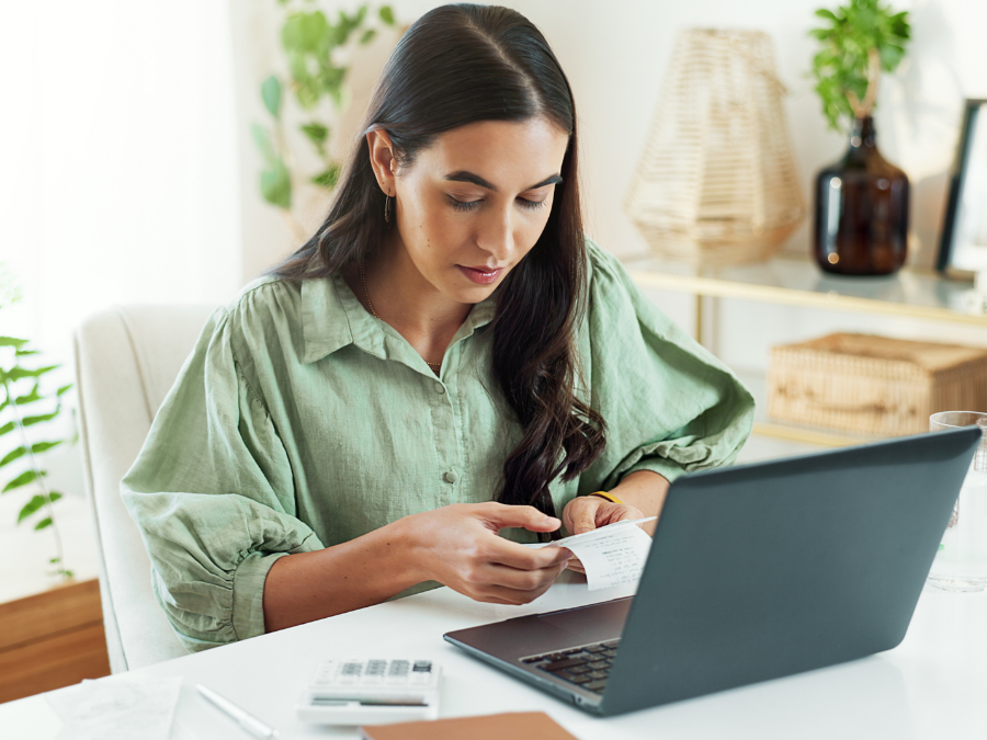 Woman sitting in front of an open laptop, holding a document while reviewing sustainability reporting information.