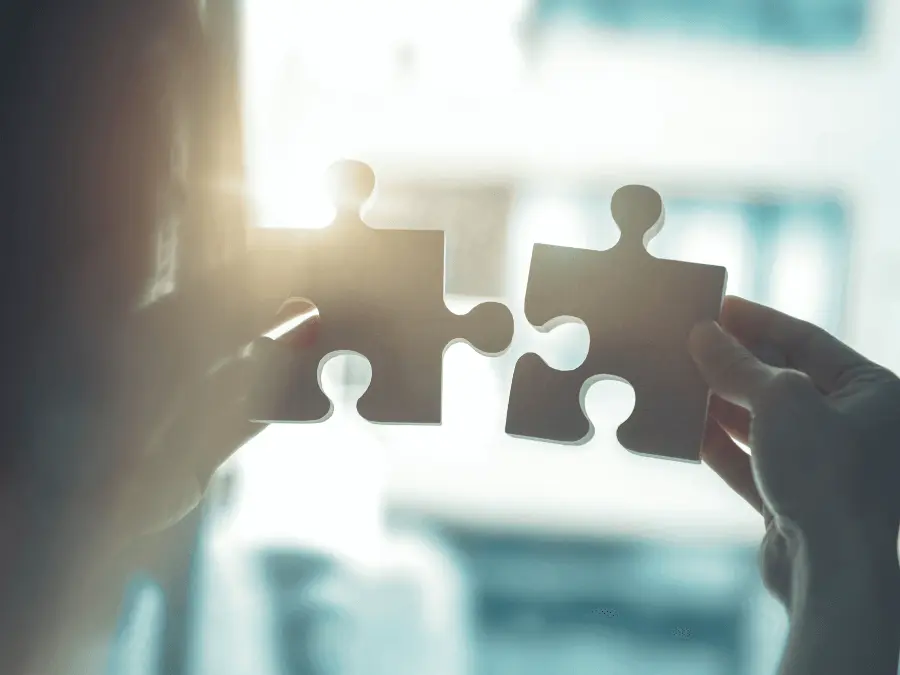 Person holding two puzzle pieces toward the light, viewed from over the shoulder