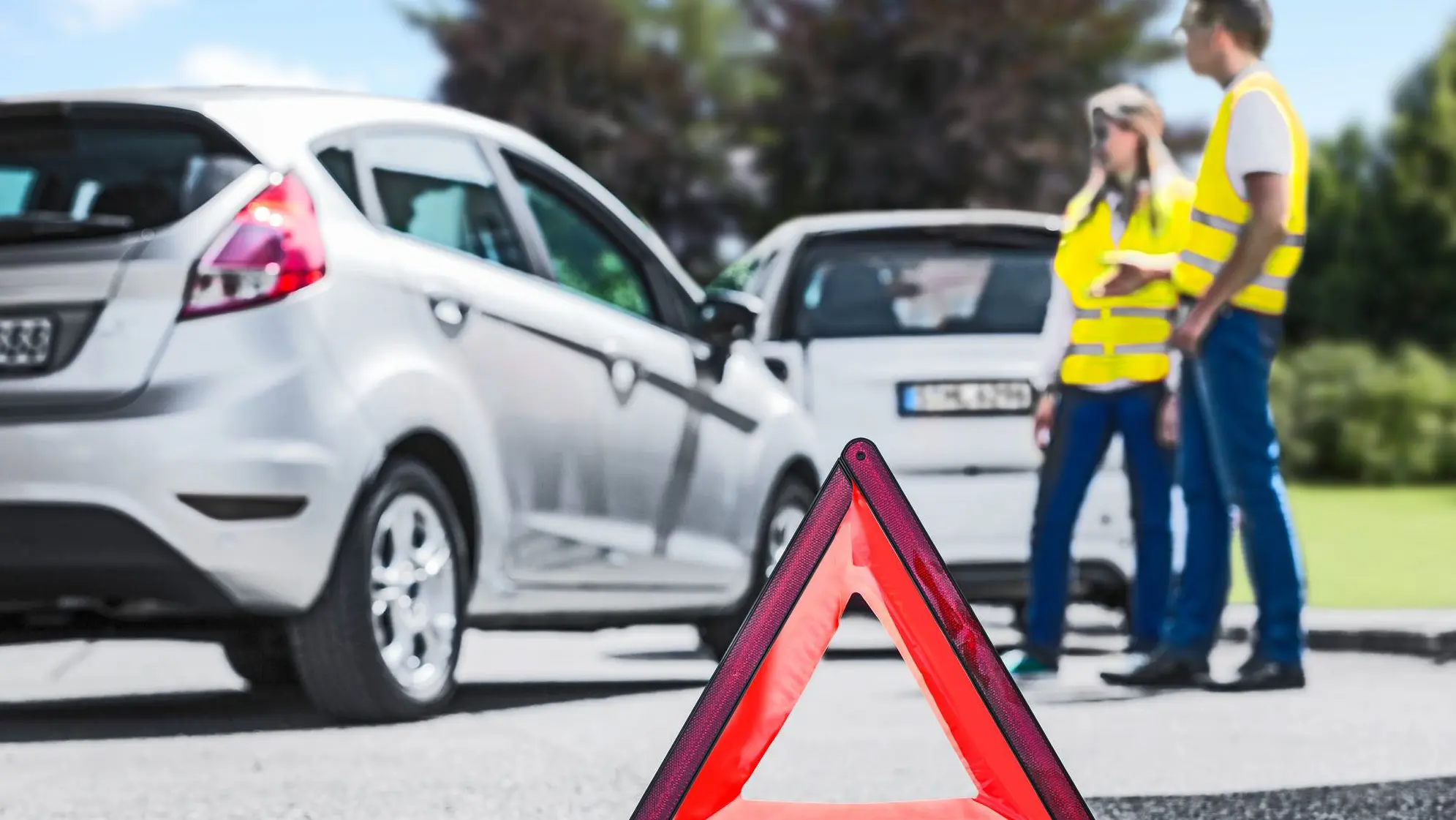 Reflecterende gevarendriehoek naast twee personenwagens aan kant van de weg