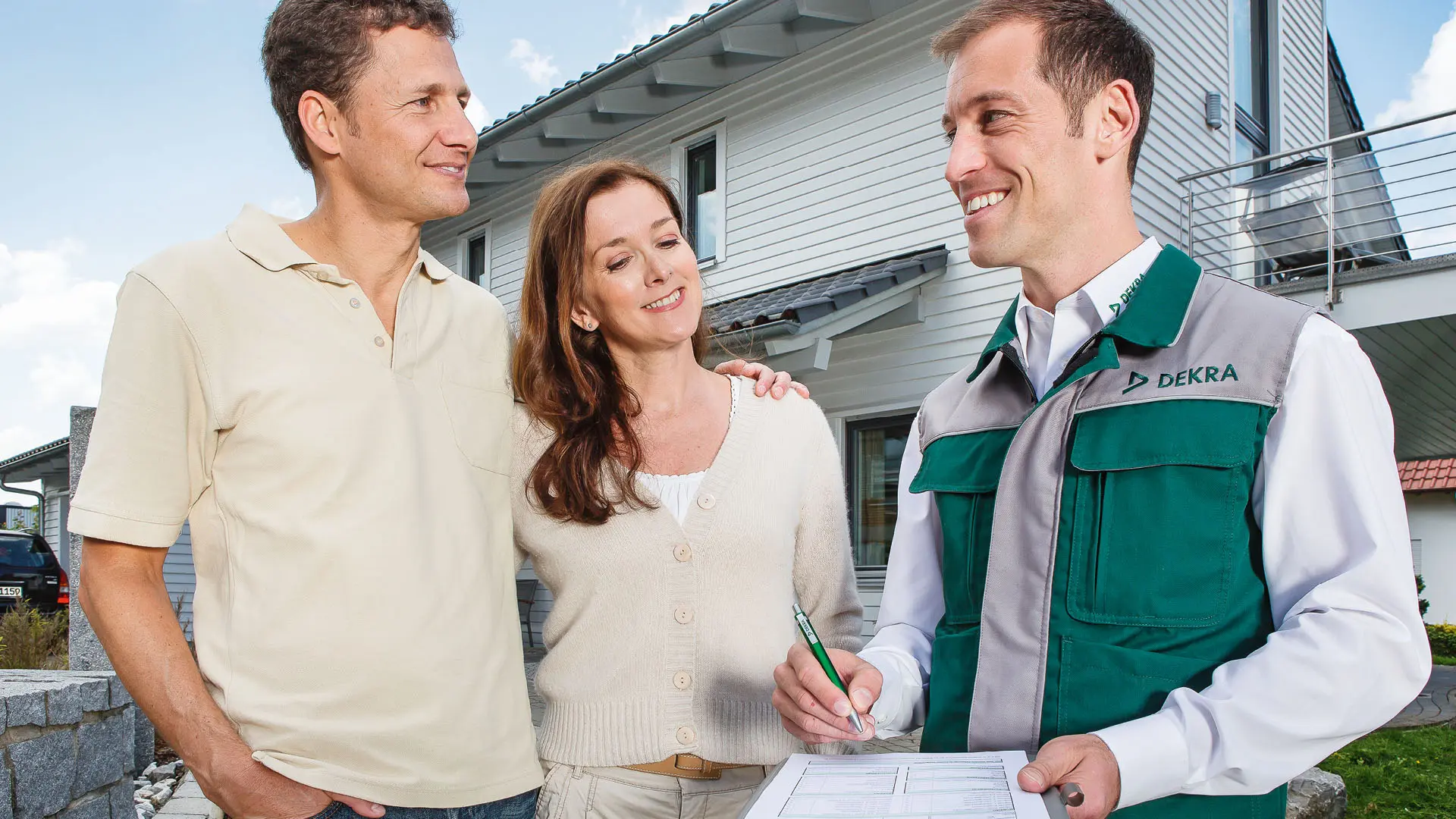 DEKRA Sachverständiger steht mit einem Paar vor Einfamilienhaus