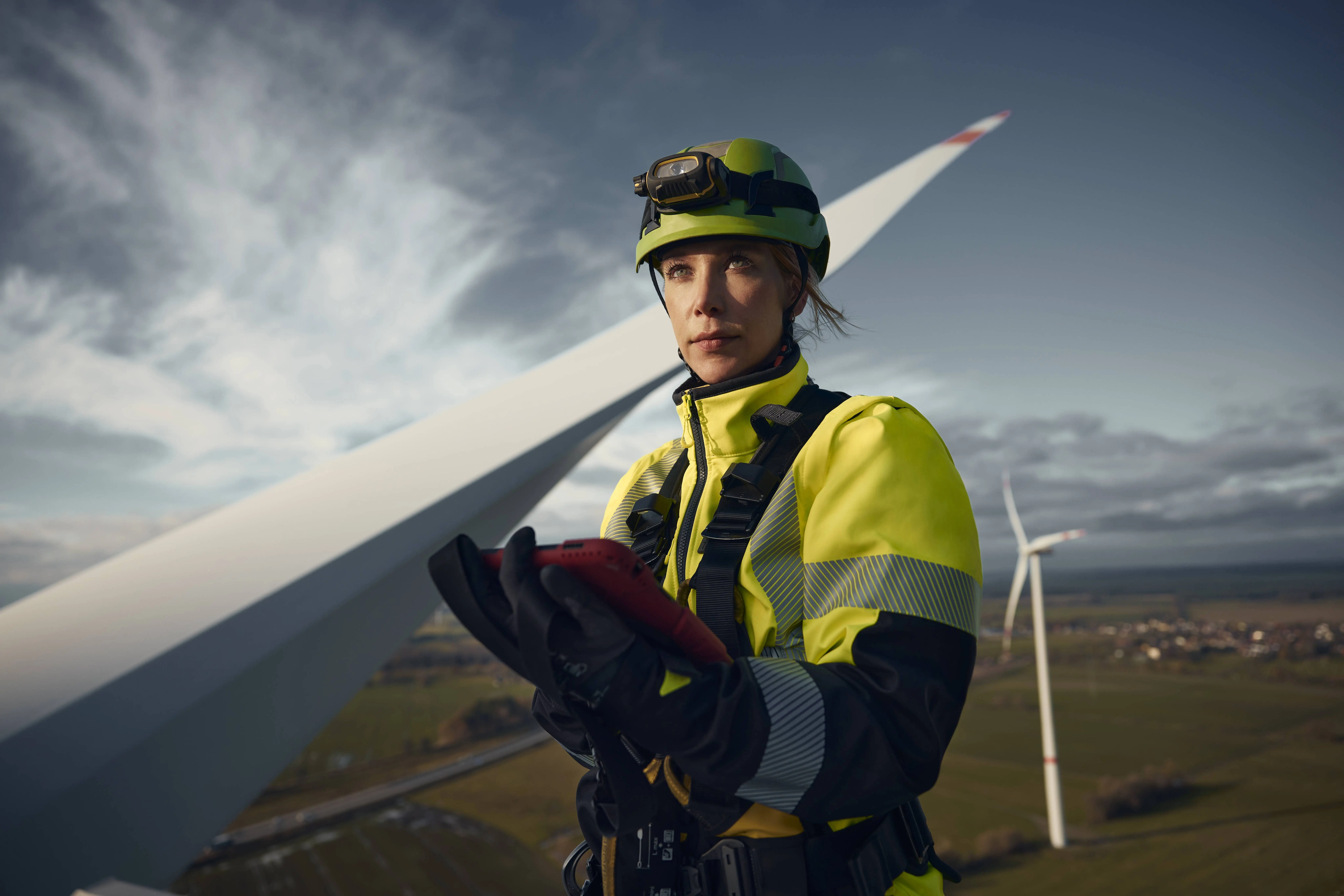 Anna-Louisa Kruse, Sachverständige für Windenergieanlagen bei DEKRA, in Arbeitskleidung und Kletterausrüstung auf einer Windkraftanlage