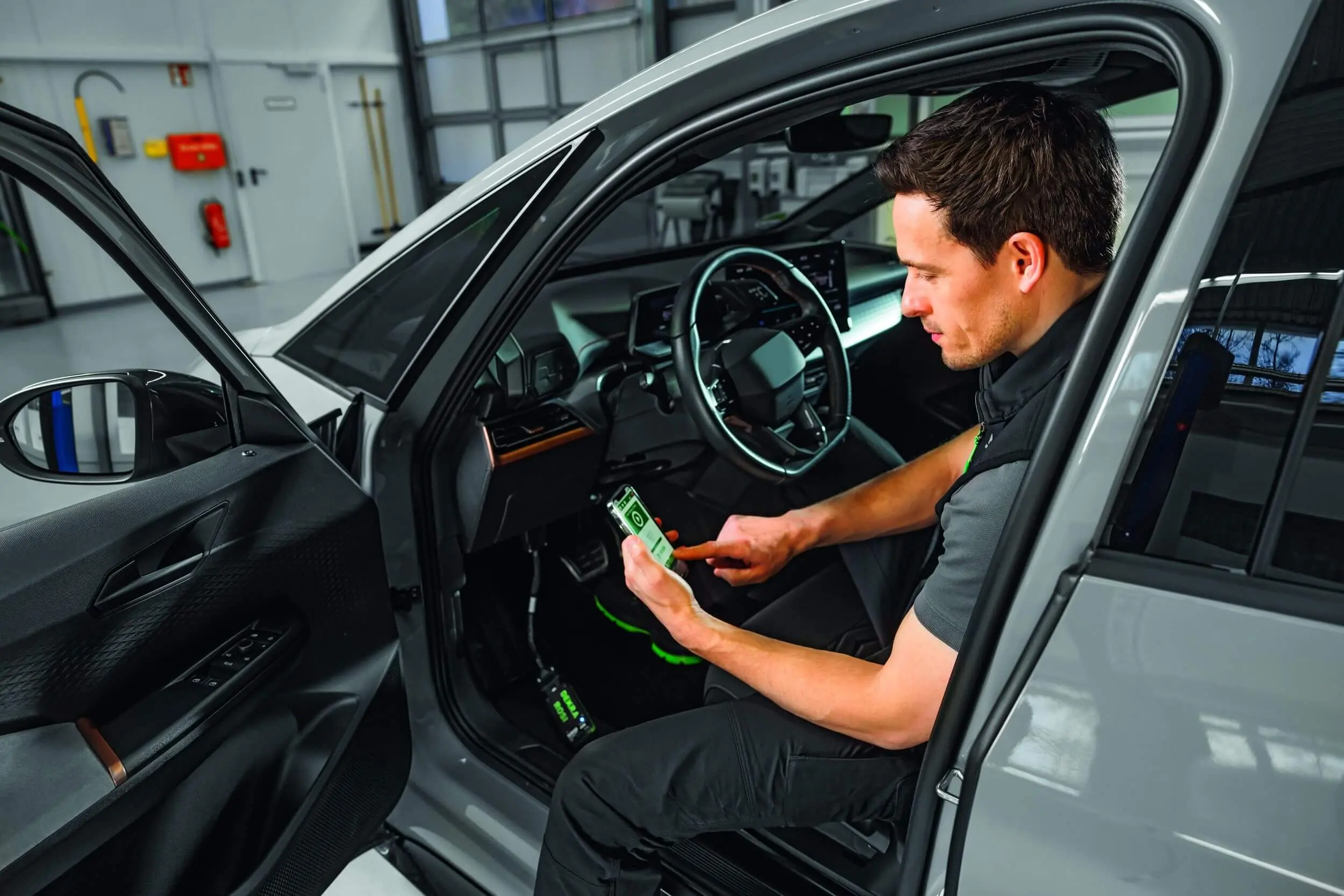 DEKRA Experte sitzt in einem Auto und sieht auf Testgerät hinab