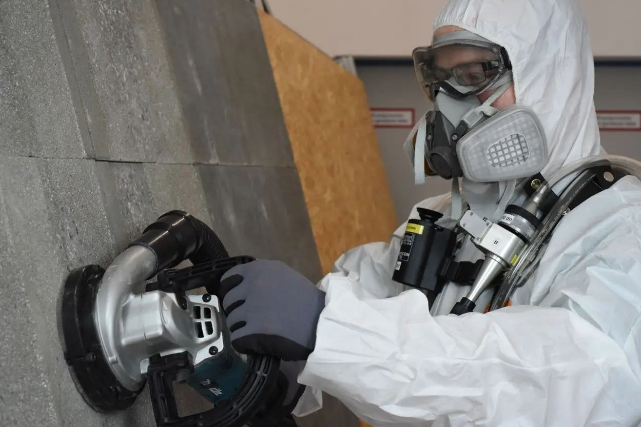 Mann in Schutzkleidung schleift einen mineralischen Untergrund ab