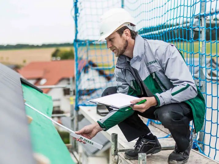 DEKRA Experte sitzt auf Gerüst und misst Dachkante mit Zollstock