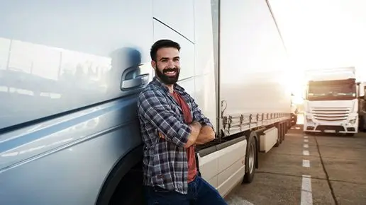 Lkw-Fahrer lehnt sich zufrieden an Lkw auf Parkplatz 