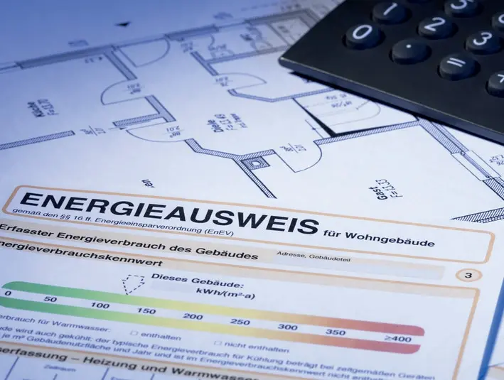 Energieausweis liegt auf Grundriss Plan neben einem Laptop