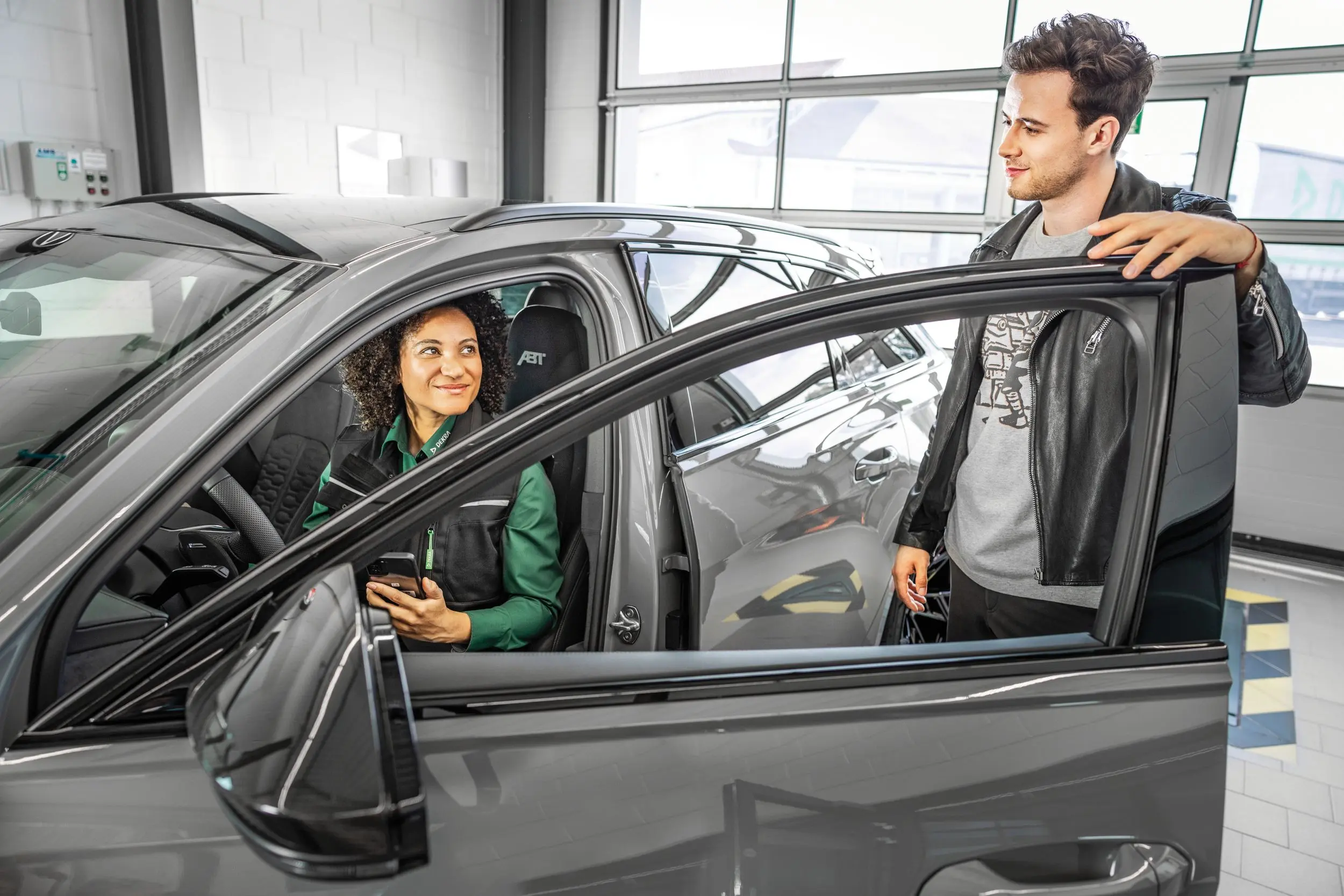 DEKRA Mitarbeiter erläutert einem Kunden etwas an geöffneter Fahrertür eines Pkw