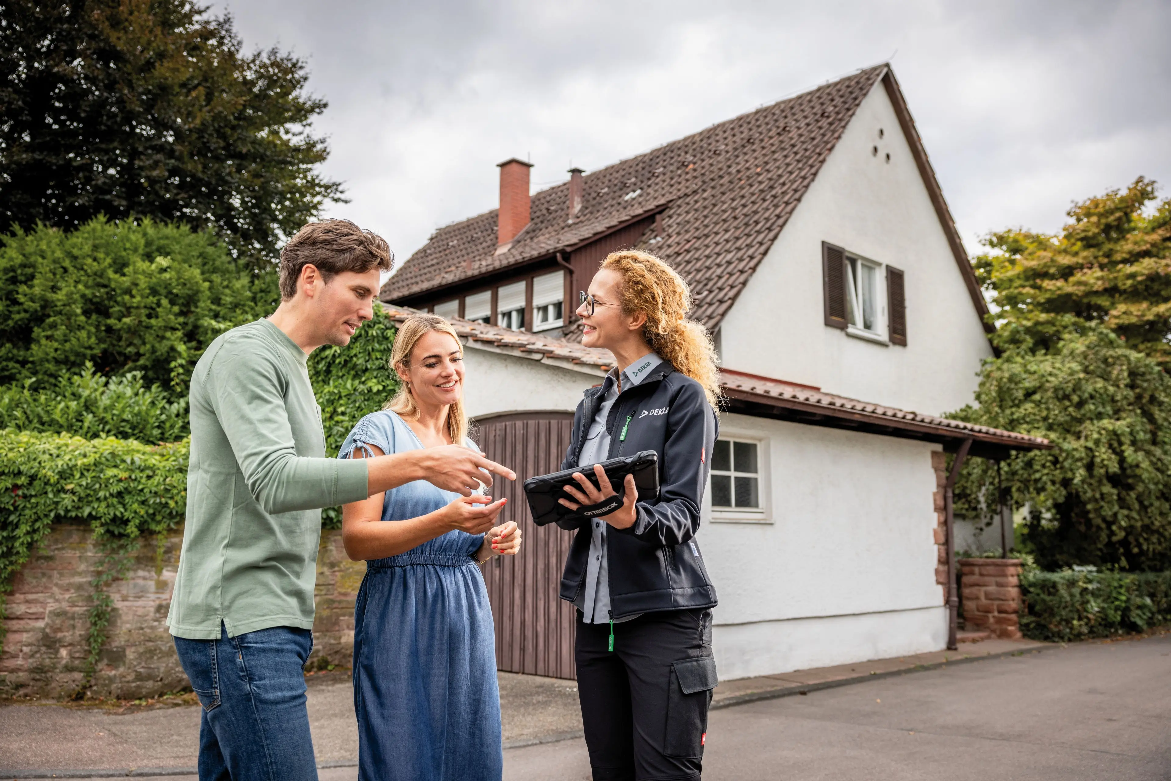 Sachverständiger mit Tablet steht mit einem Paar vor einem Einfamilienhaus
