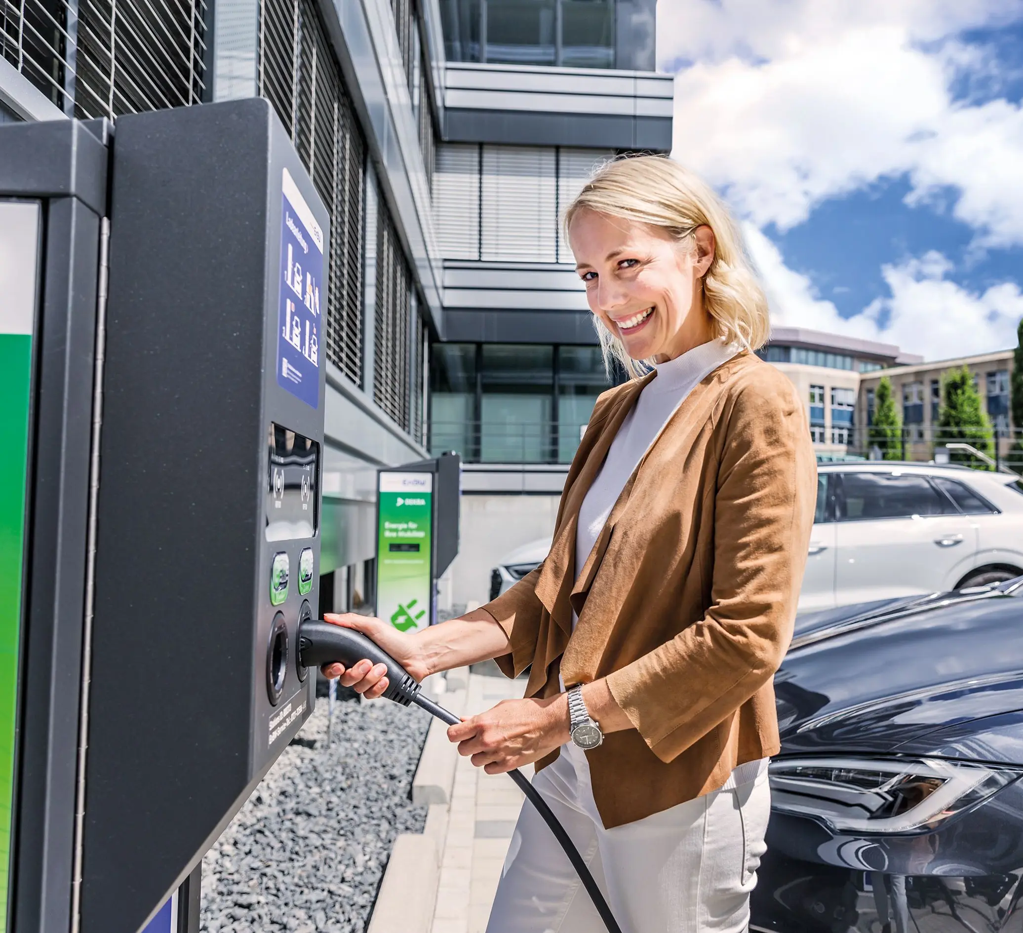Frau an E-Ladesäule mit Ladekabel in der Hand