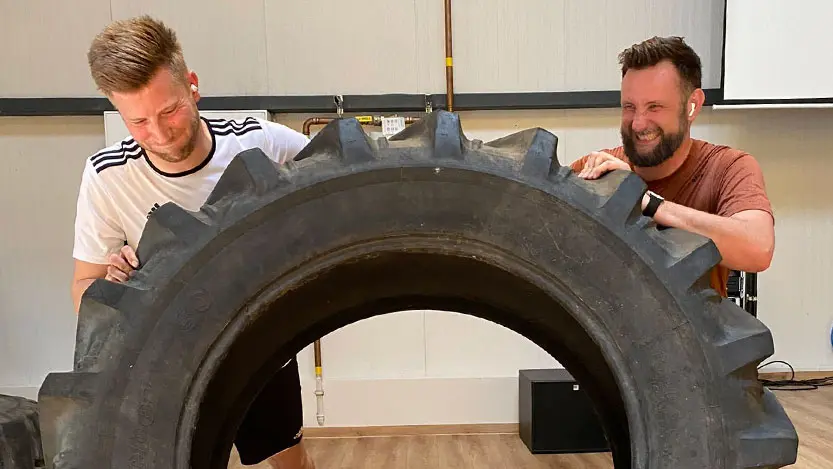 Zwei Personen beim Heben eines schweren Reifens Zwei Personen beim Heben eines schweren Reifens