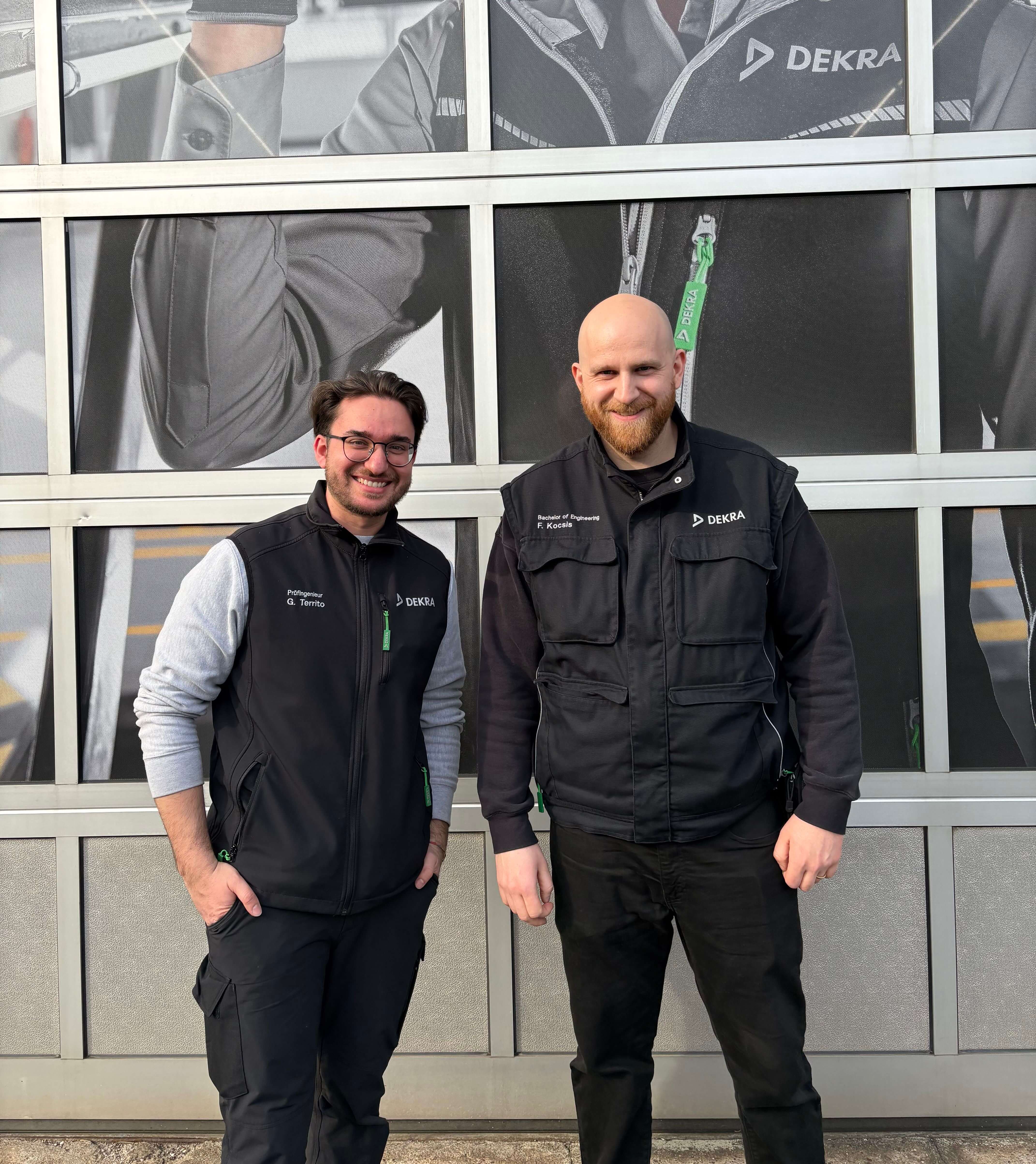 Girolamo & Florian in Arbeitskleidung vor dem Tor einer DEKRA Prüfhalle