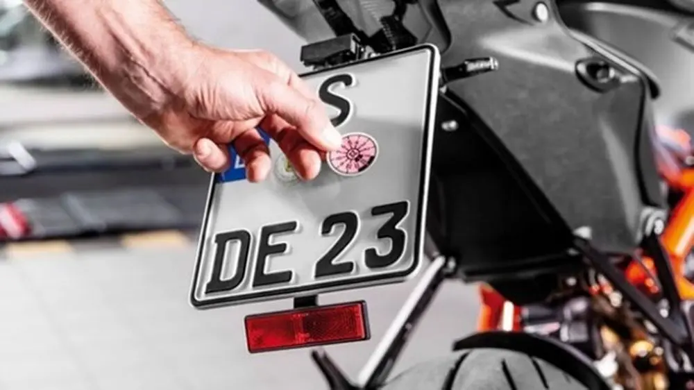 Mensch klebt HU-Prüfplakette auf Motorradnummernschild