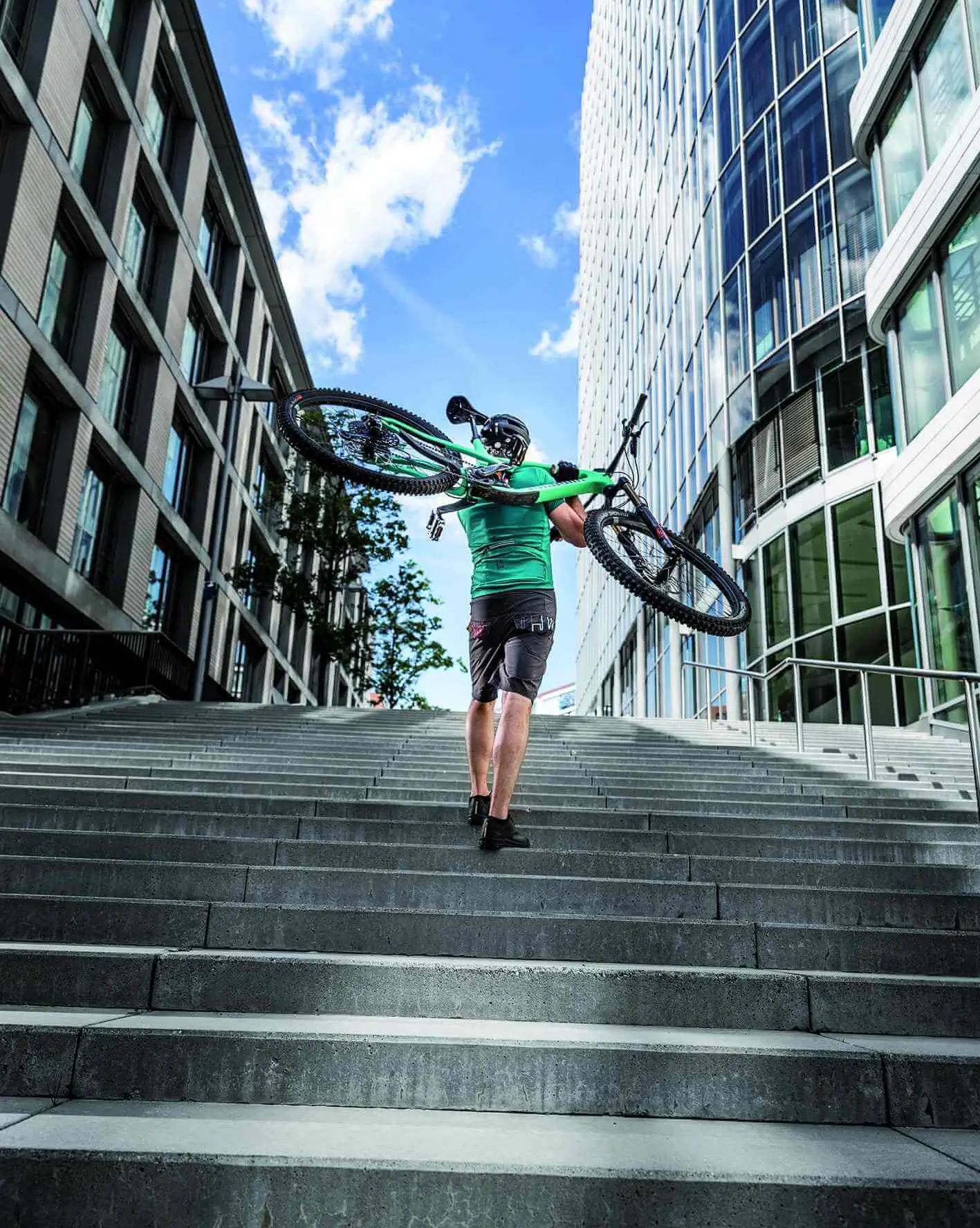 Mann trägt Fahrrad auf Schulter und läuft eine Treppe hoch