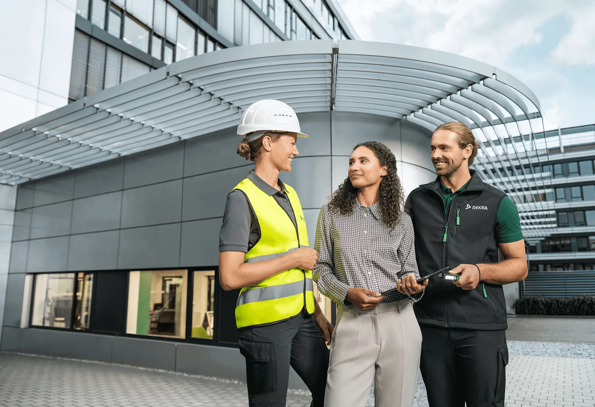 Drei Mitarbeitende in Arbeits- und Businesskleidung lächeln sich an Drei Mitarbeitende in Arbeits- und Businesskleidung lächeln sich an