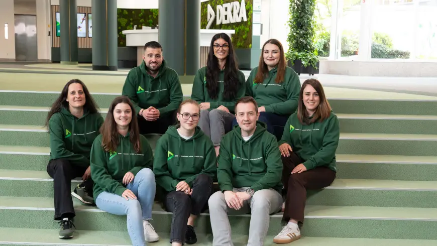 Recruiterinnen und Recruiter sitzen lächelnd auf einer Treppe im DEKRA Empfangsbereich