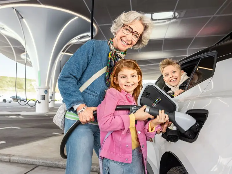 Frau mit zwei Kindern beim Aufladen eines E-Autos