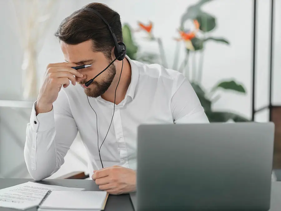 Mann sitzt am Schreibtisch und fasst sich an seine Stirn