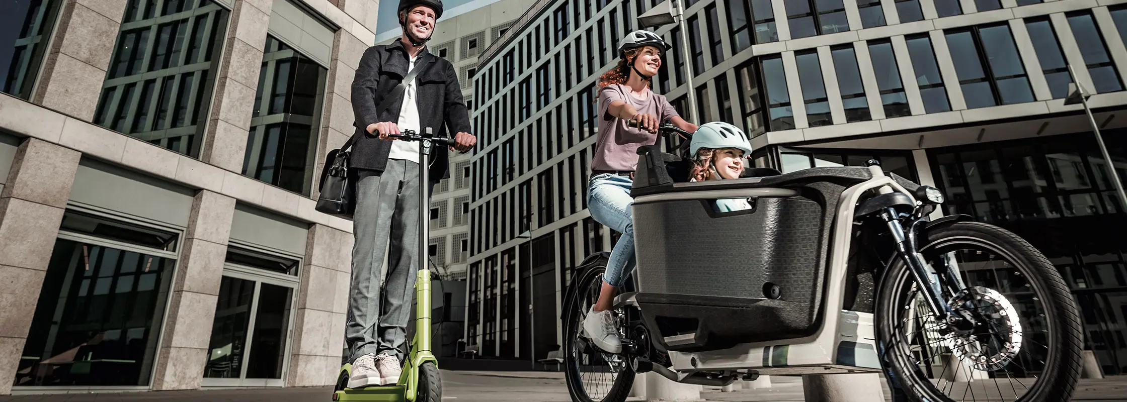A man riding an E-Scooter and a women with her kid on an electrical cargo bike