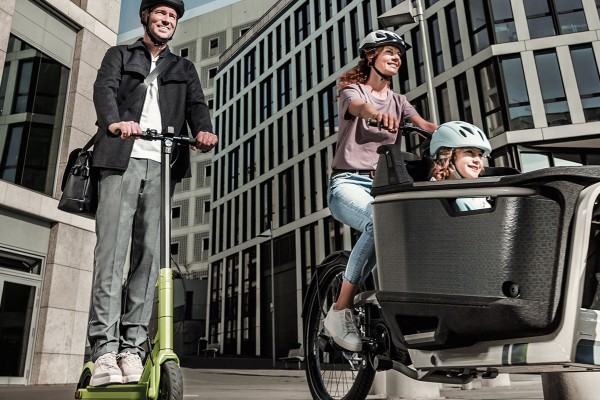 A man riding an E-Scooter and a women with her kid on an electrical cargo bike