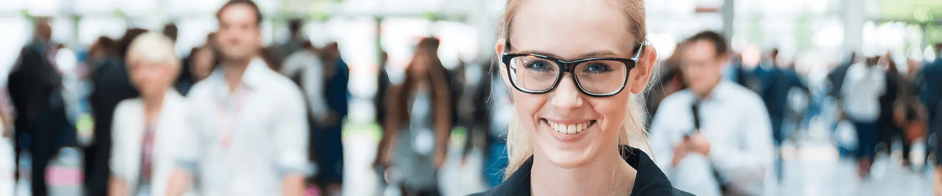 A smiling woman facing the camera, with attendees wearing accreditation badges visible in the background.