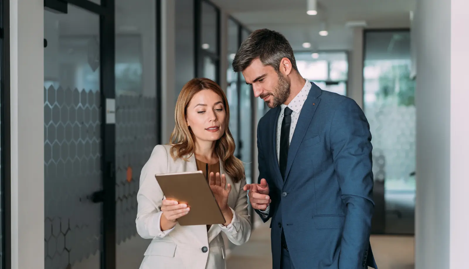 Two colleagues discussing and reviewing content on a tablet held by the woman in a business setting. Two colleagues discussing and reviewing content on a tablet held by the woman in a business setting.