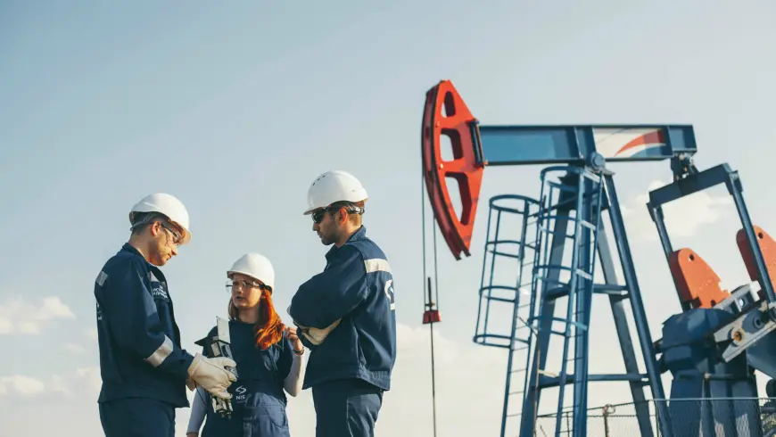  A woman and two men, all in work clothes featuring helmets and overalls, standing at a site