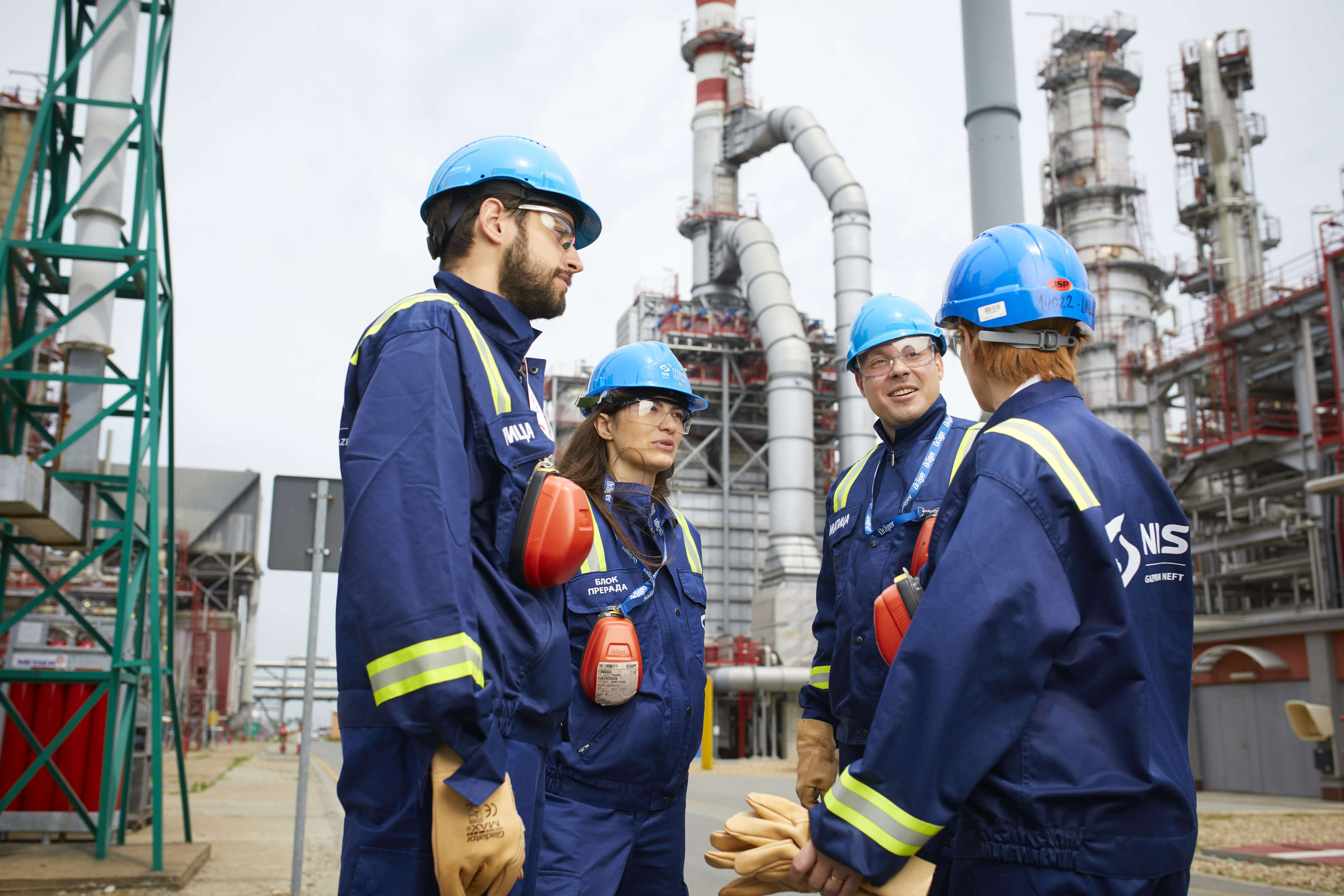 Four people in NIS overalls, with helmets and safety googles discussing