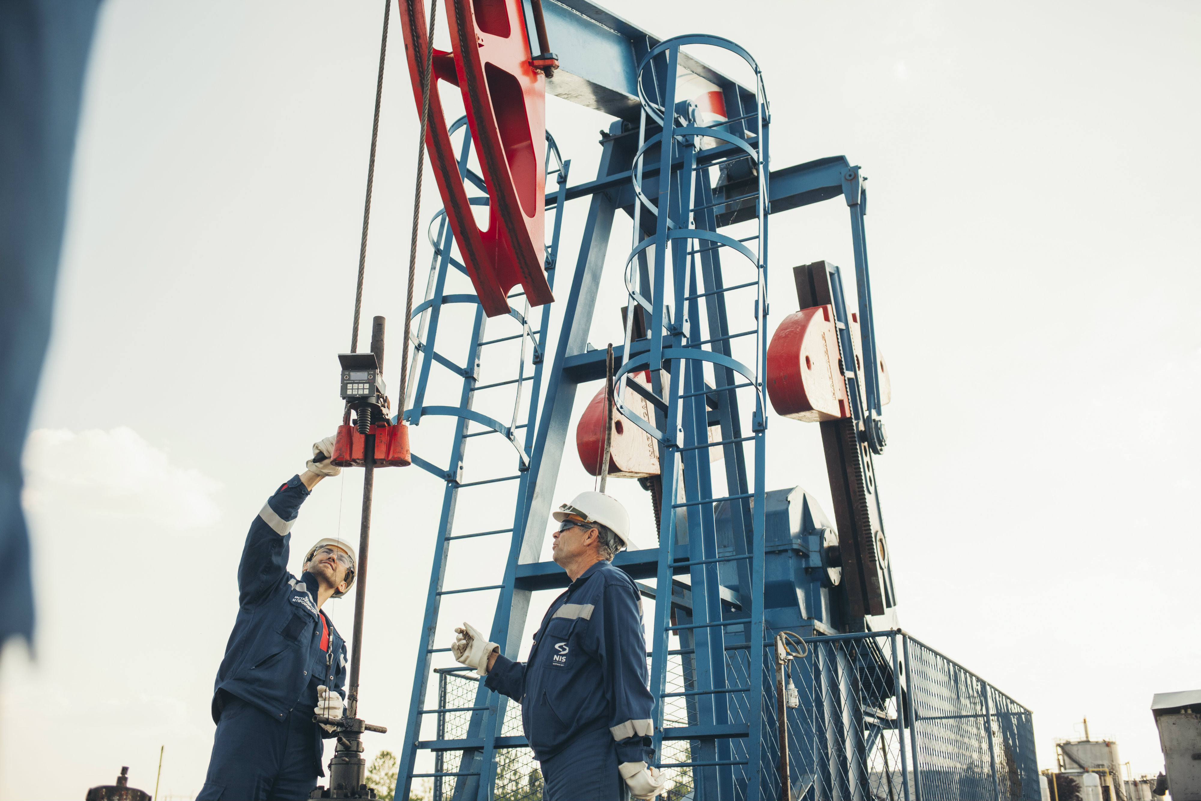 Two men in overalls and safety gear handling a drill