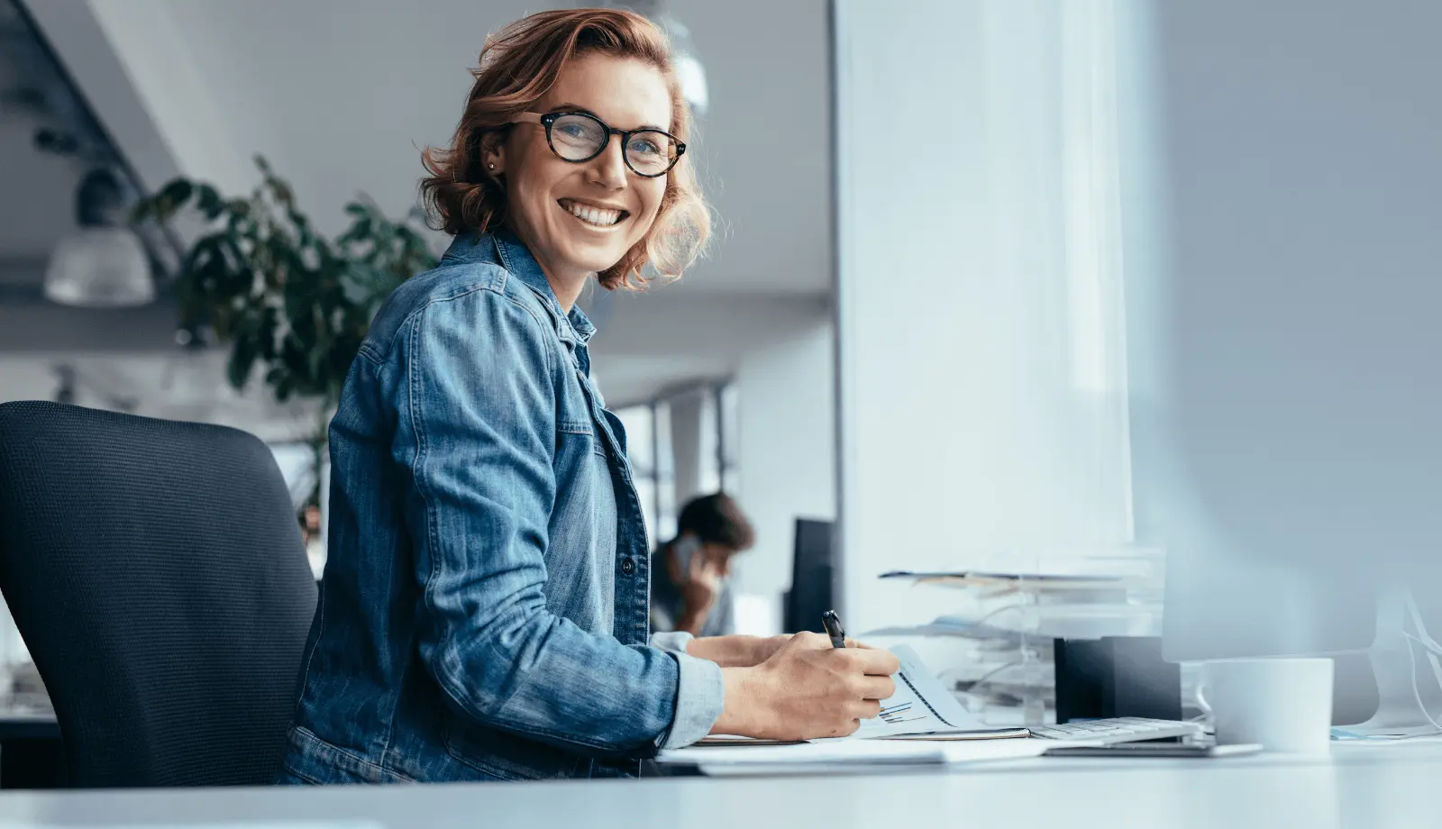 A woman is sitting at a desk smiling at the camera.